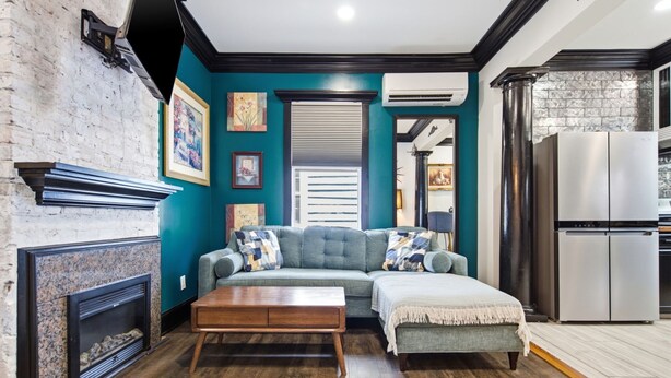 A living room with a fireplace, a sofa set, a coffee table, and a kitchen area with a refrigerator. - The Jade Getaway in Historic Castle St. District (Wilmington)