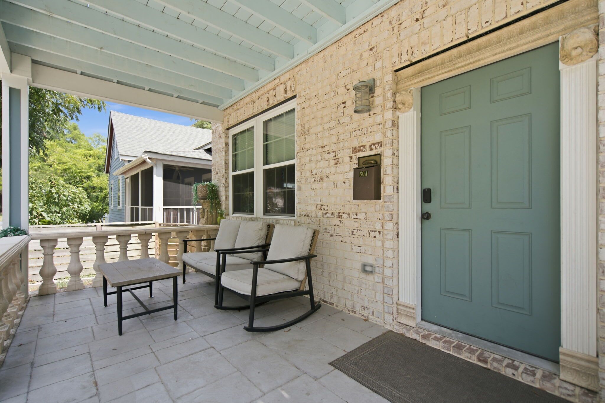 A covered porch with a bench and chairs, a mailbox, and a green door.