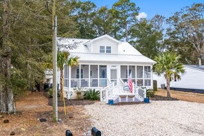A two-story house with a porch, a flag, and a sign indicating it is a beach house. - Cozy Beach Cottage Near Ocean Isle Beach (Ocean Isle Beach)