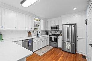 A modern kitchen with white cabinetry, stainless steel appliances, and a wooden floor. - Cozy Beach Cottage Near Ocean Isle Beach (Ocean Isle Beach)