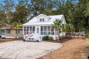 A two-story house with a covered porch, a flag, and a small flagpole. - Cozy Beach Cottage Near Ocean Isle Beach (Ocean Isle Beach)