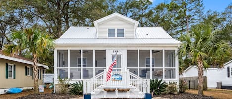 A white building with a covered porch, a flag, and a sign indicating the year 1940.