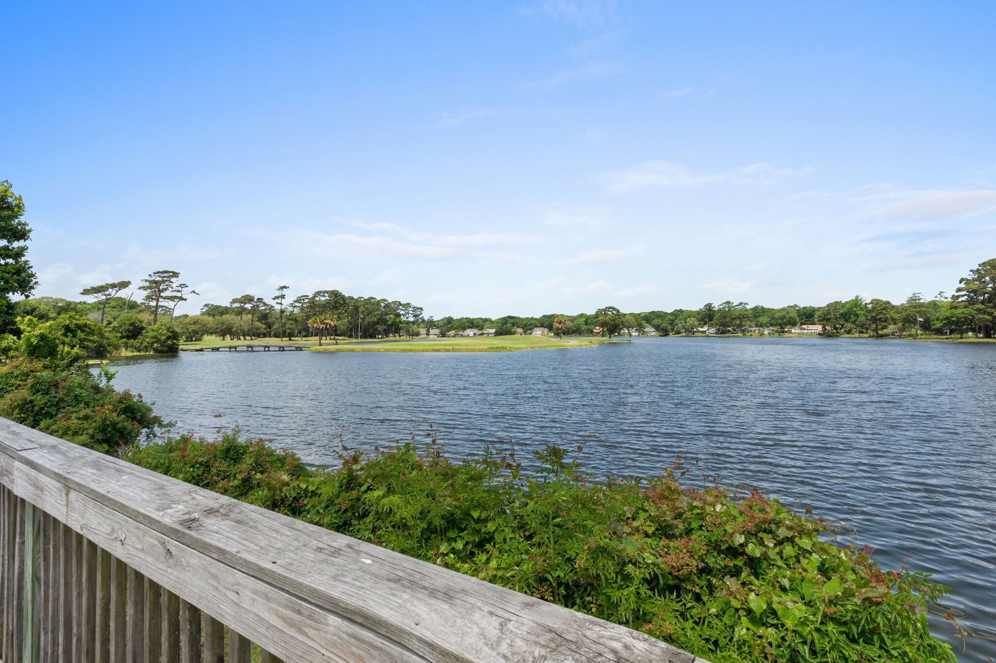 Ein ruhiger See mit einem Holzdeck im Vordergrund und ein Park mit Bäumen und Häusern im Hintergrund.