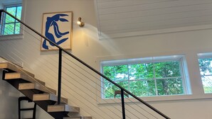 Eine moderne Treppe mit Holzstufen und schwarzen Geländern, die zu einer Empore mit einem gerahmten Kunstwerk und einer Wandleuchte führt.