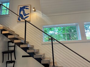 Eine moderne Treppe mit Holzstufen und schwarzen Geländern, die zu einer Empore mit einem gerahmten Kunstwerk und einer Wandleuchte führt.