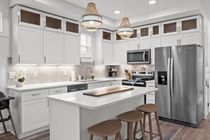 Une cuisine moderne avec des meubles blancs, des appareils en acier inoxydable, un îlot central doté de tabourets et un éclairage suspendu.