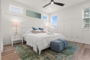 Une chambre à coucher avec un lit, des tables de chevet, un ventilateur de plafond et une fenêtre avec des stores.