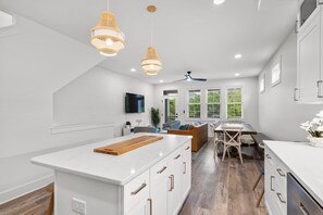 Une cuisine moderne dotée d’un îlot central, de luminaires suspendus et d’un coin repas offrant une vue sur la verdure.