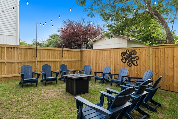 A backyard with a wooden fence, outdoor seating with chairs and a table, and string lights. - Rooftop Spa + Bar | Walk to Beach | Sleeps 15! (Carolina Beach)
