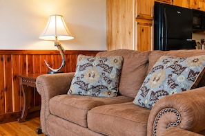 A brown sofa with floral patterned cushions, a wooden wall, and a black refrigerator. - River View Cabin on the White River (Calico Rock)