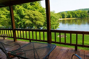 A wooden deck with a metal table and chairs, overlooking a lake with trees and hills in the background. - White River Views, Covered Porch Cabin (Calico Rock)