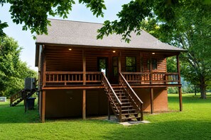 Eine zweigeschossige Blockhütte mit Balkon, Treppe und einer kleinen Veranda.