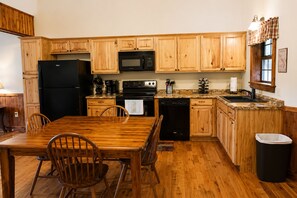 Une cuisine avec des meubles de rangement en bois, un réfrigérateur noir, un four à micro-ondes, un lave-vaisselle et une table à manger avec des chaises.