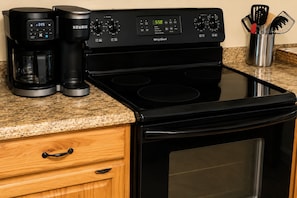 A kitchen with a black stove, a Keurig coffee maker, and a Whirlpool coffee maker. - River View Cabin on the White River (Calico Rock)