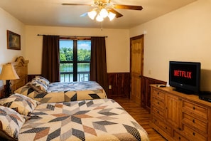 A hotel room with two beds, a TV, a ceiling fan, and a window with a view of a lake. - River View Cabin on the White River (Calico Rock)