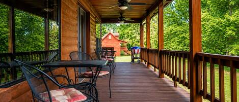 Una terraza cubierta de madera con mobiliario exterior, una parrilla de barbacoa y vista a un edificio rojo a lo lejos.