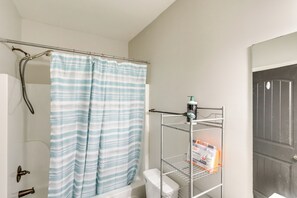 Ein Badezimmer mit Duschvorhang, Toilette, Ablagefläche für Toilettenartikel und einer Tür.