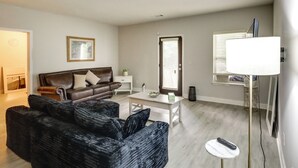 A living room with a brown leather sofa, a black armchair, a white coffee table, and a TV stand with a flat-screen TV. - Shop, Dine & Hike: Lawrenceville Home By Parks (Lawrenceville)