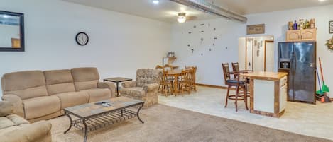 A living room with a sofa, coffee table, dining table, chairs, and a kitchen area with a refrigerator.