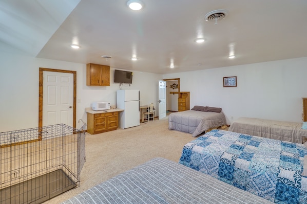 A bedroom with two beds, a desk, a television, and a small kitchenette.