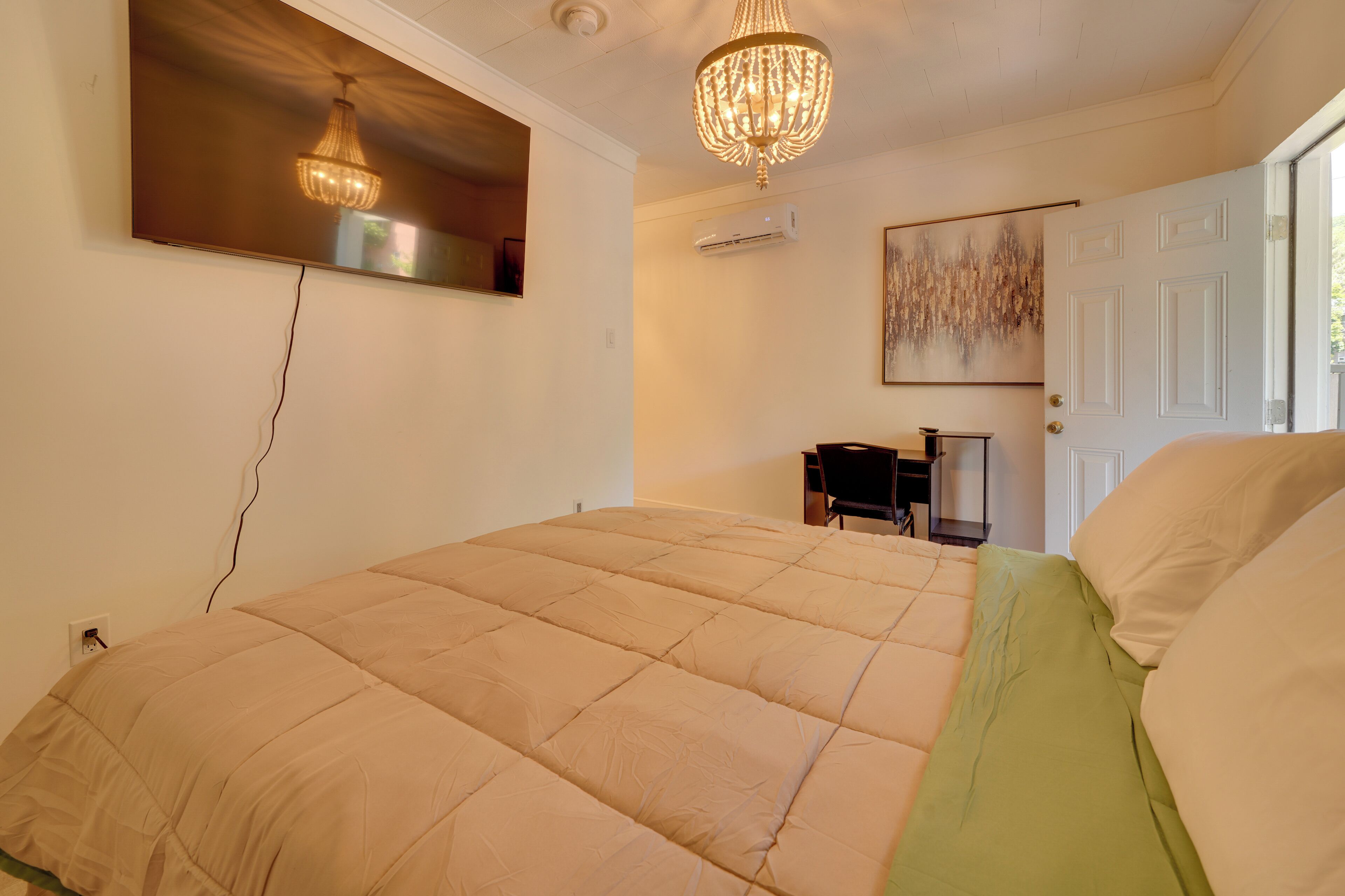 Un dormitorio con cama, candelabro, equipo de aire acondicionado, puerta y un cuadro en la pared.