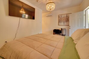 A bedroom with a bed, a chandelier, an air conditioning unit, a door, and a painting on the wall.