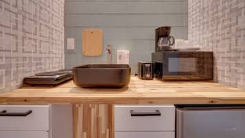 A kitchen with a wooden countertop, a large brown bowl, a coffee maker, and a microwave. There are two white drawers and a wooden cutting board on the wall.