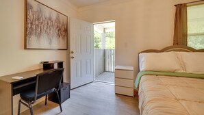 Ein Schlafzimmer mit Schreibtisch, Stuhl, Bett und einer Tür, die auf einen Balkon führt.