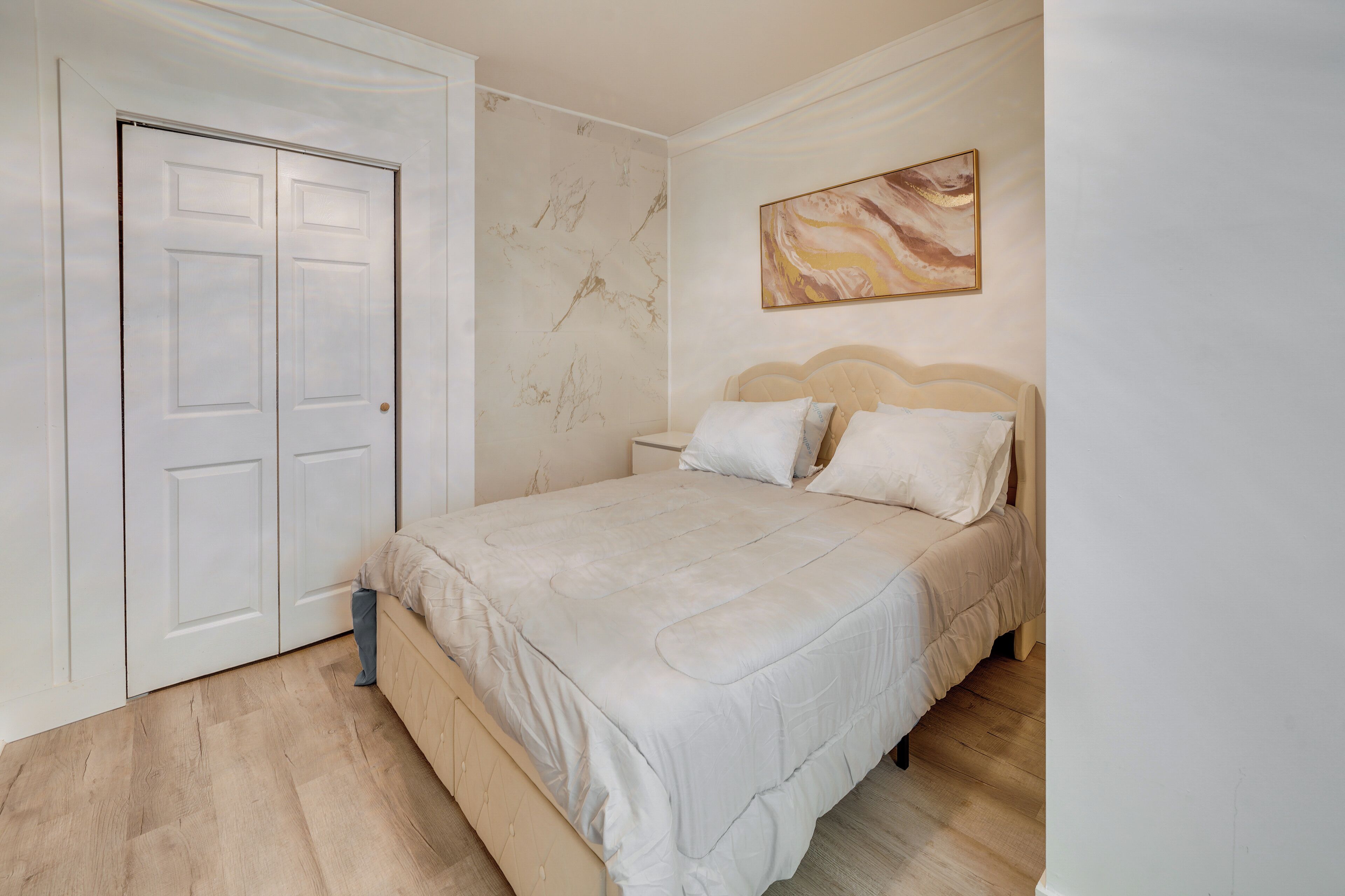 A bedroom with a bed, a nightstand, a door, and a wall with a painting.