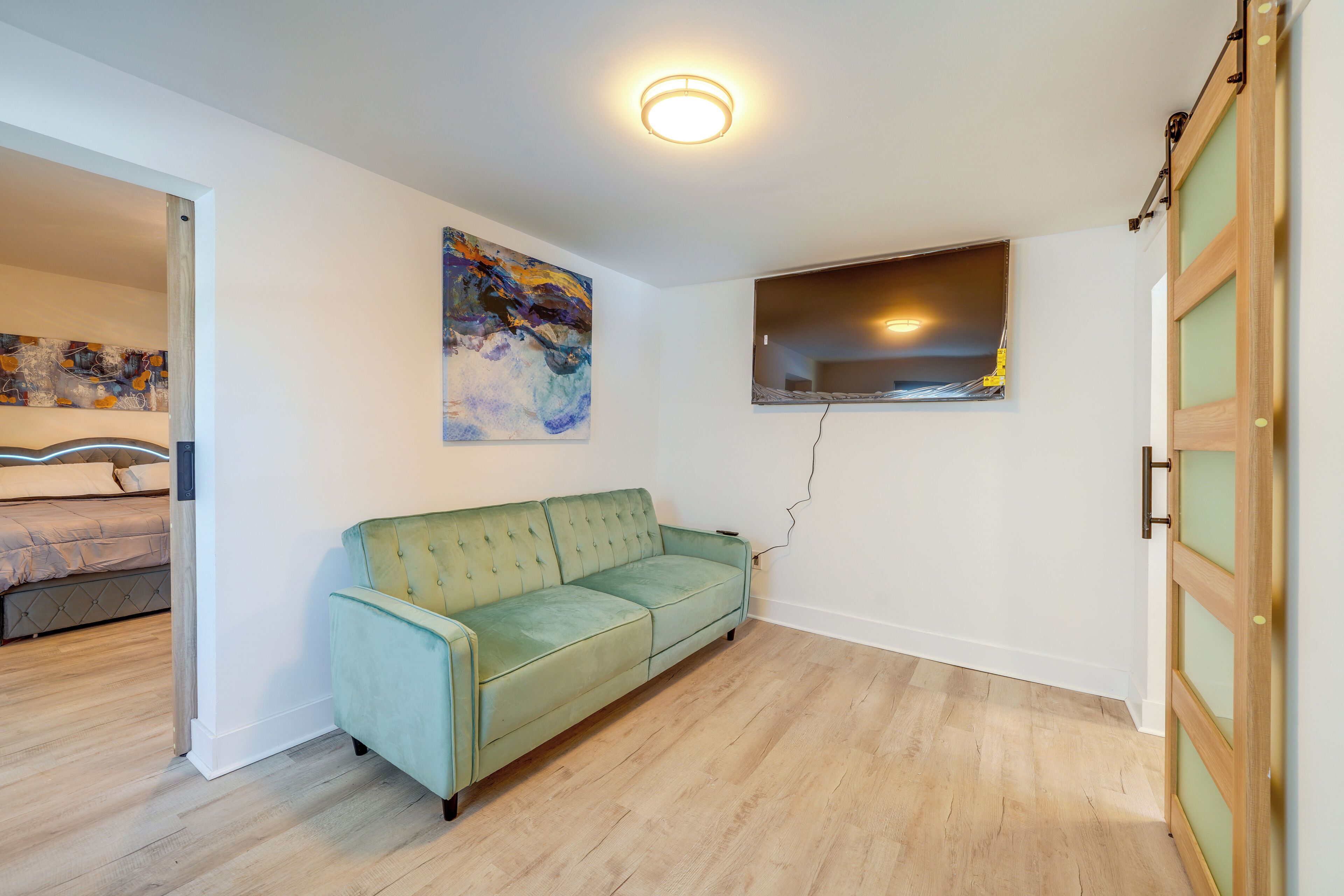 Ein Zimmer mit einem grünen Sofa, einem Bild an der Wand, einem Fenster und einer Holztür.