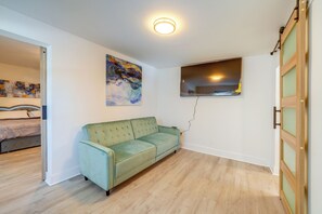 A room with a green sofa, a painting on the wall, a window, and a wooden door.