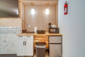 A compact kitchen with a wooden countertop, a microwave, a coffee maker, and a trash bin.