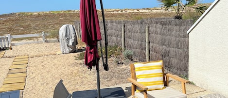 Un espace patio aménagé avec une table, des chaises, un parasol rouge et un banc en bois.