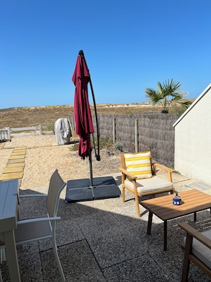 Eine Terrasse mit Tisch, Stühlen, einem roten Sonnenschirm und einer hölzernen Bank.