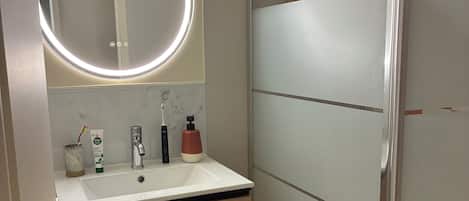 A bathroom with a white sink, wooden cabinet, and a glass shower enclosure.