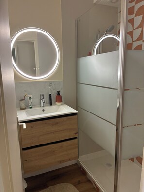 Ein Badezimmer mit weißem Waschbecken, Holzschrank und einer Duschkabine aus Glas.