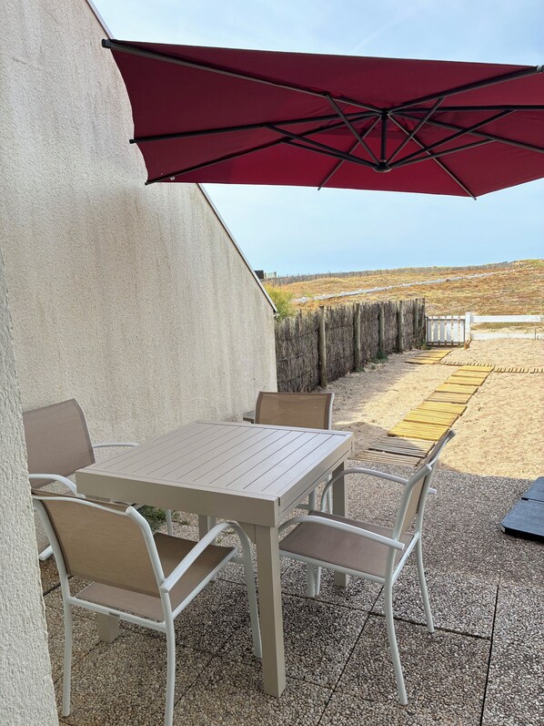 Eine Terrasse im Freien mit Tisch und Stühlen, einem roten Sonnenschirm und Blick auf einen Zaun und die Landschaft.