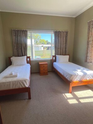 A hotel room with two single beds, a wooden nightstand, a small dresser, and a window with curtains.