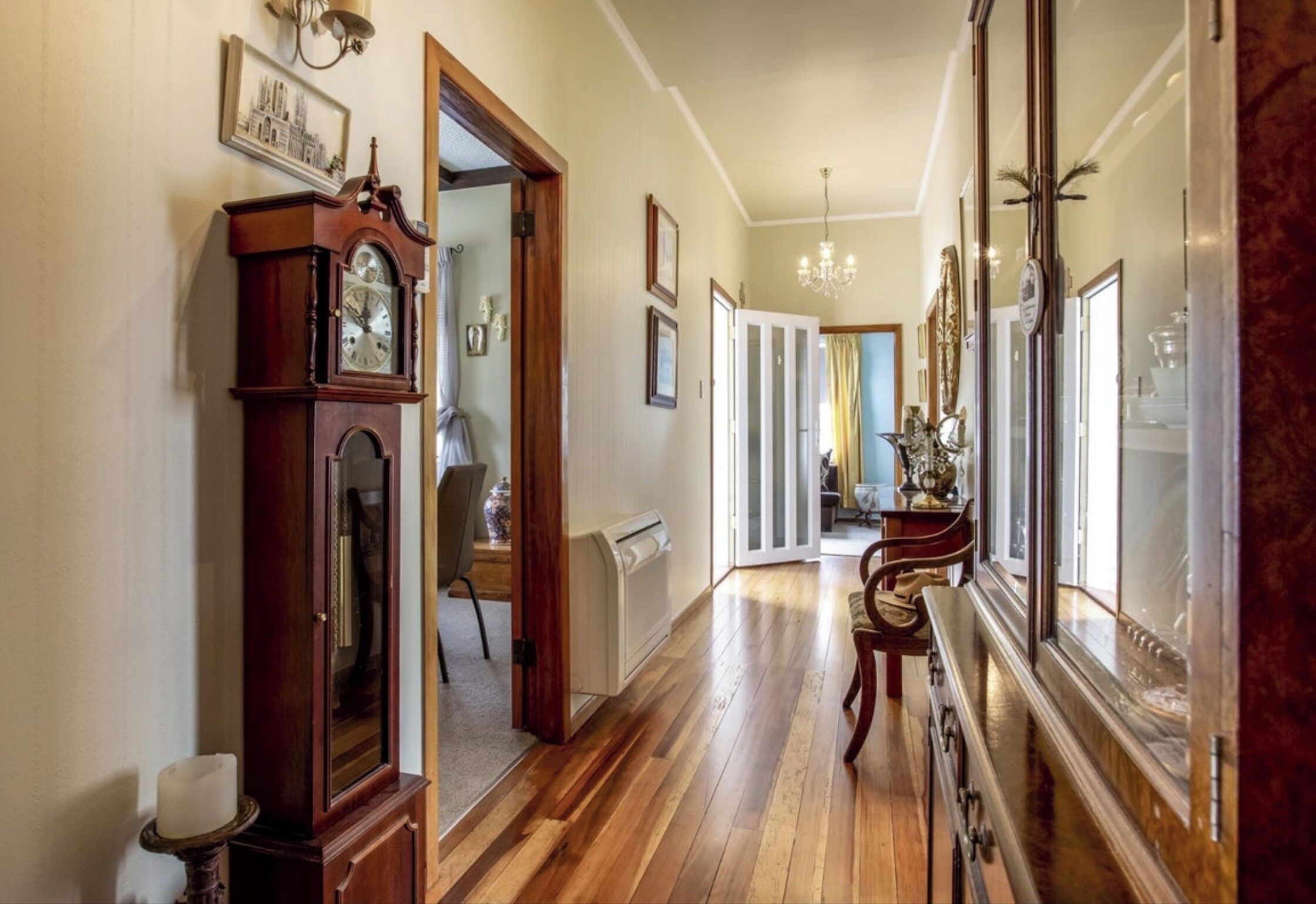 A hallway with wooden flooring, a grandfather clock, and a mirror reflecting the room.