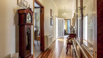 A hallway with wooden flooring, a grandfather clock, and a mirror reflecting the room.