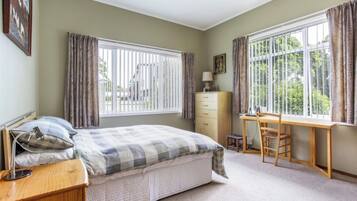 A bedroom with a bed, a desk, a chair, a dresser, and a window with curtains.