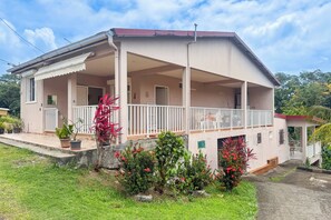 A two-story building with a covered porch and a small garden area with potted plants and flowers. - Le Lamentin - Patio - TV (Le Lamentin)