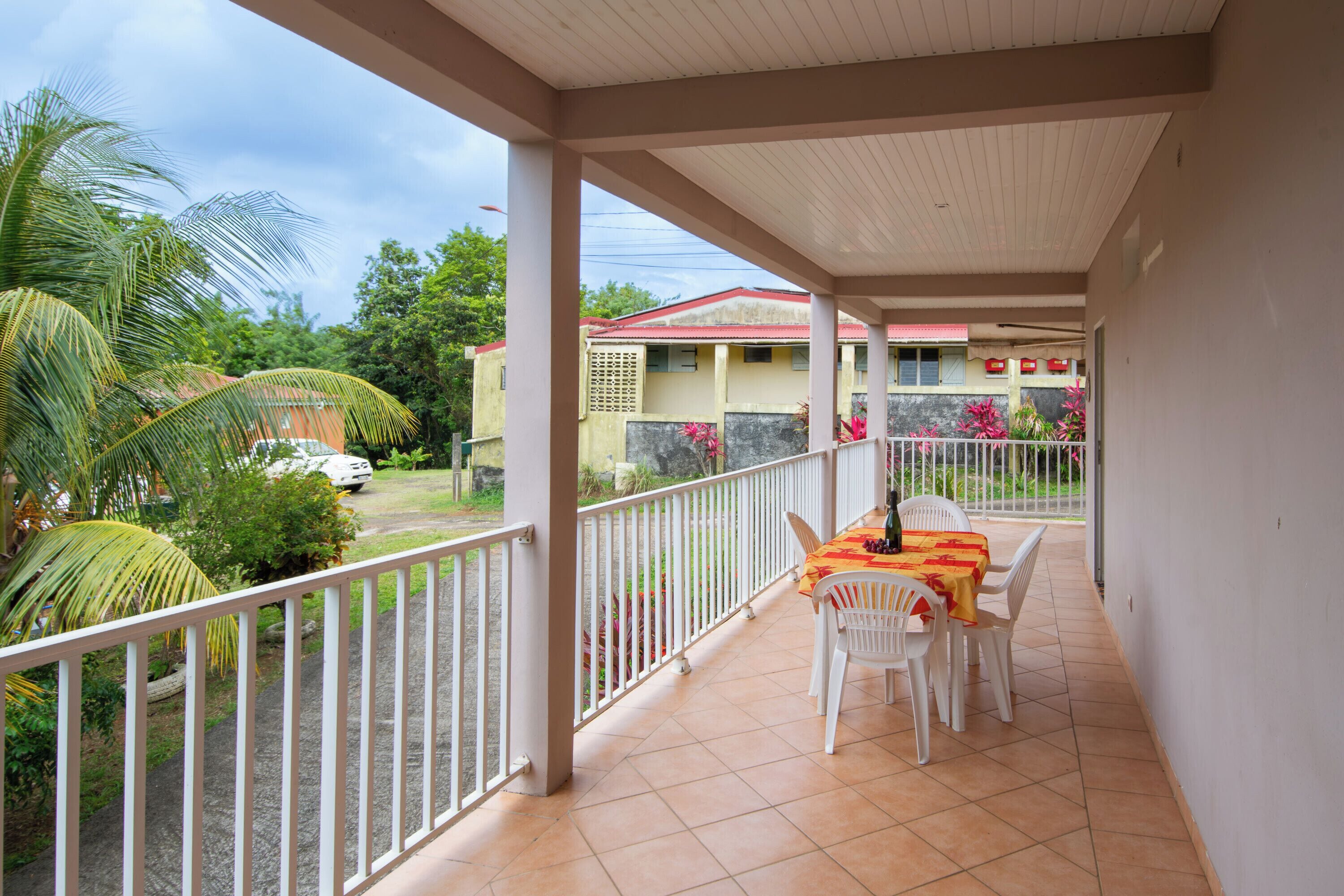 A covered balcony with a table and chairs, a view of a residential area, and a car parked outside.