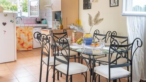 Comedor con mesa de vidrio, sillas de metal negro y cocina al fondo.