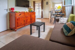 Un salon comprenant un canapé, une table basse, un téléviseur et un coin cuisine avec un meuble et une table.