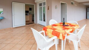 Un comedor con una mesa preparada para cuatro personas, sillas de plástico blanco y una botella de vino sobre la mesa.
