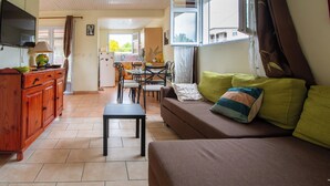 Una sala de estar con sofá, una mesa de comedor y sillas. Hay un televisor en la pared.