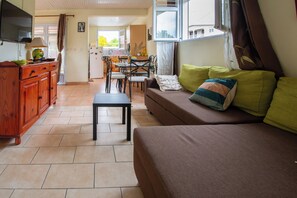 Ein Wohnzimmer mit einer Couch, einem Esstisch und Stühlen. An der Wand ist ein Fernseher.