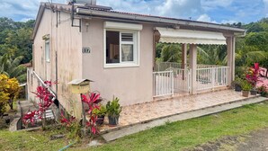 Una casa de un piso con un porche cubierto, un buzón y un pequeño jardín con plantas tropicales.
