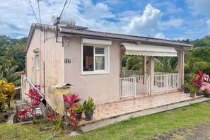 Ein einstöckiges Haus mit Veranda, Briefkasten und einem kleinen Garten mit tropischen Pflanzen.